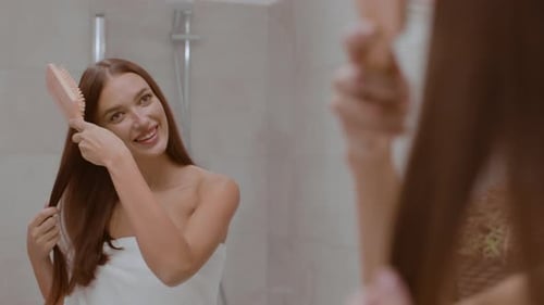 Woman Smiles, Brushing Hair in Bathroom Mirror