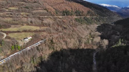 Aerial: passenger train going through a valley in a mountainous landscape and snow covered peaks in