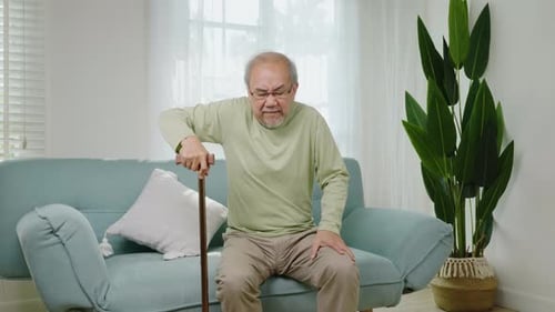 Asian senior old man with eyeglasses type to standing up from sofa with walking cane stick