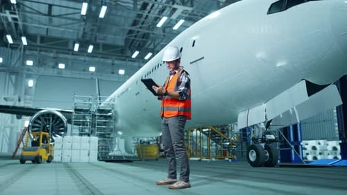 Asian Male Engineer Working On A Tablet While Aircraft Maintenance