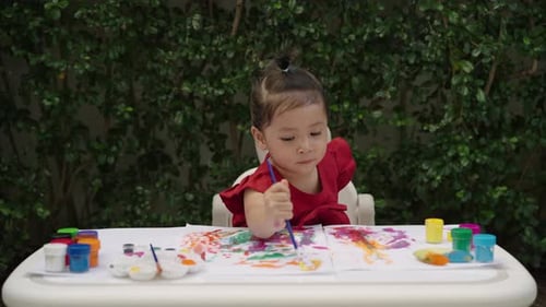 happy toddler girl painting watercolor in a paper at backyard