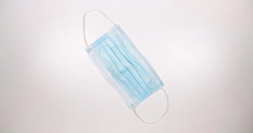 Hand Places Blue Surgical Mask on White Surface