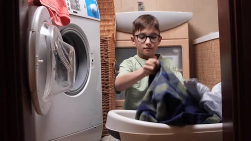 Junge mit Brille lädt schmutzige Kleidung in eine moderne Waschmaschine und macht Hausarbeiten