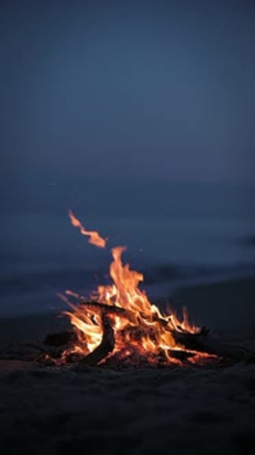A Campfire Burns on a Deserted Sandy Beach at the Seashore in the Evening