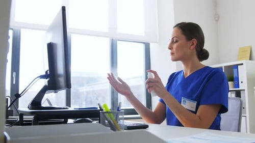 Hispanic female doctor sprays hand sanitizer at hospital with computer on table