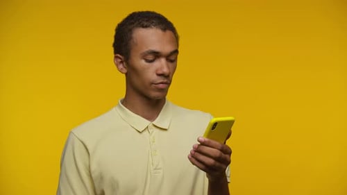 Young Adult Using Smartphone on Yellow Background
