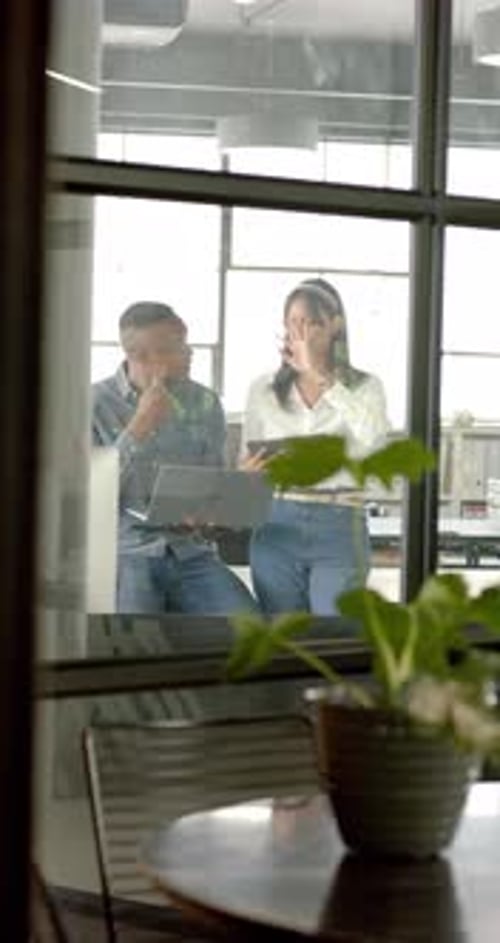 Vertical video: Discussing project, business colleagues using laptop in modern office setting