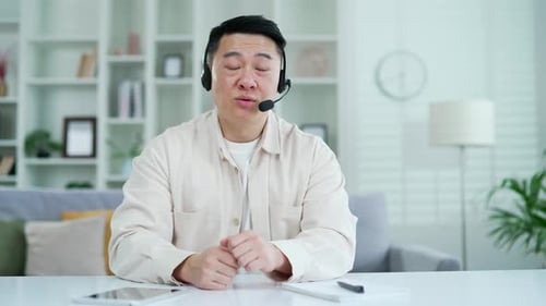 Webcam view. Confident asian man in headset talking on video call on laptop while sitting in home