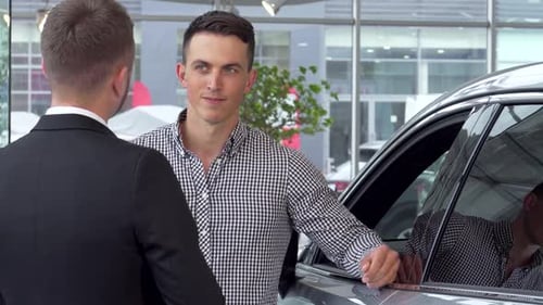 Confident Man Shaking Hands with Car Salesman at a Modern Dealership