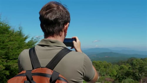 Man with Backpack Photographing Scenic Landscape on Sunny Day Travel