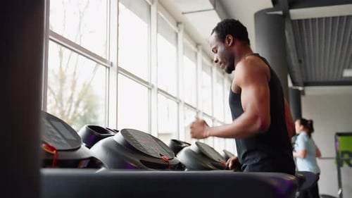 Young African Man in Sportswear Running on Treadmill at Gym