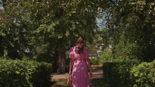 Caucasian Lady Walking Along Bright Garden Trail at Leisurely Pace Portrait of Stylish Woman in Pink