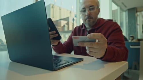 Homem usando cartão de crédito para compras on-line em laptop e smartphone no café