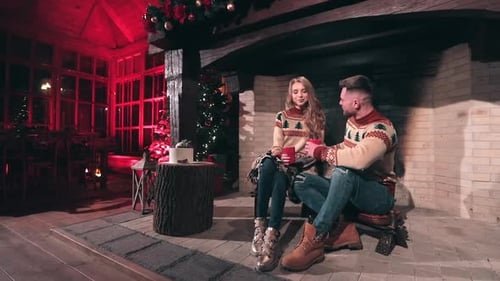Romantic couple in knitted Christmas sweaters. Young man and woman sitting near the fireplace
