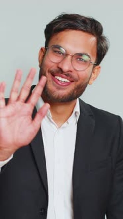 Smiling man waving hello wearing suit and glasses