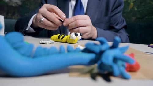 Closeup Man Makes Plasticine Stripes for Toy Bee at Table