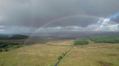High aerial drone footage in the rain rolling left above a long, straight road looking towards a bir