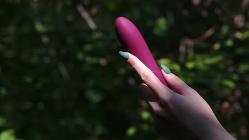 Close-up of female hands holding a purple dildo for female masturbation against the background of gr Close-up of female hands holding a purple dildo for female masturbation against the background of gr