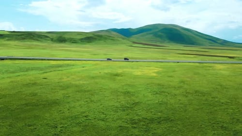 Shooting from drone shows highway among mountains of meadows. Car rushes