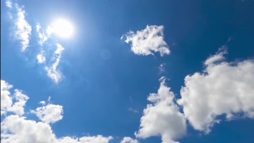 Bright sun shining in blue sky. Quickly flying white clouds against the sun. View from below.