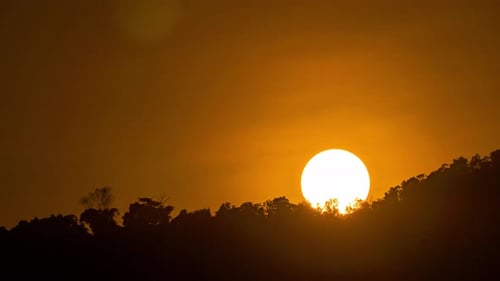 Timelapse de um pôr do sol dramático com céu laranja em um dia nublado.