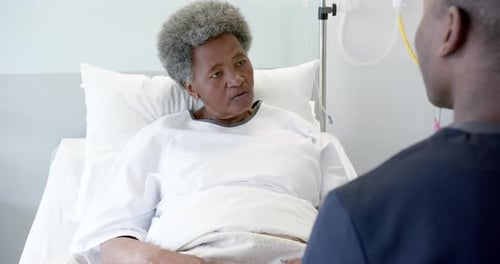 African american male doctor talking with female senior patient in hospital room, slow motion