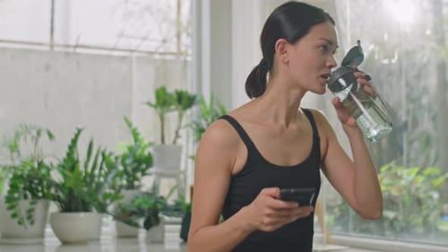 Woman Drinking Water While Using Mobile Phone