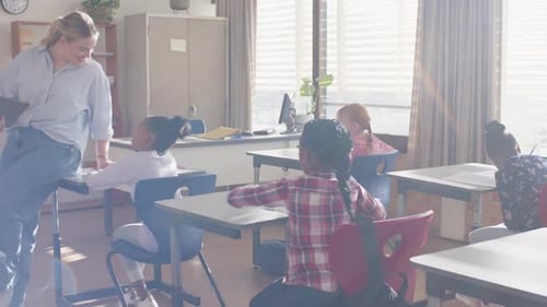 In school, female teacher interacting with students in classroom, holding tablet
