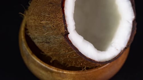 Coconut rotates on a black background in a wooden bowl. Cracked fresh coconut top view with splash