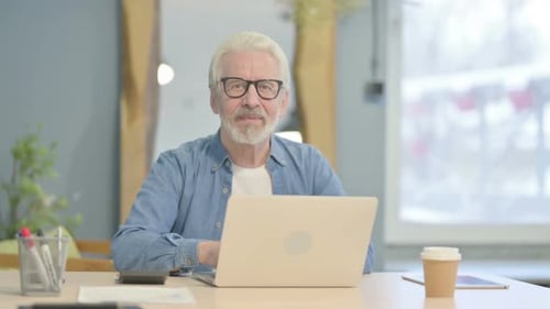Senior Man Giving Thumbs Up at Desk with Laptop