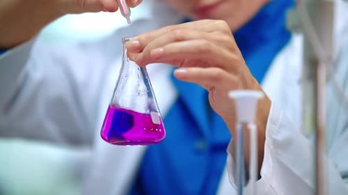 Scientist adds liquid to flask in laboratory