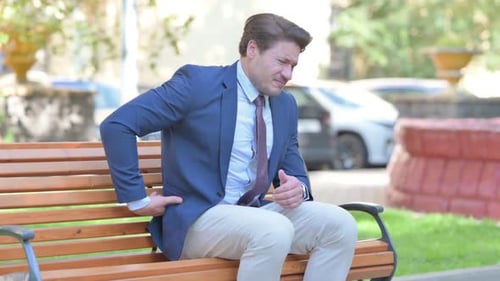 Man in Pain on Park Bench Rubbing Back