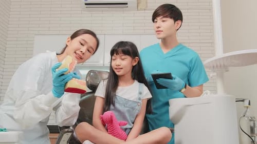 An Asian female dentist demonstrates a toothbrush to a girl in dental clinic.