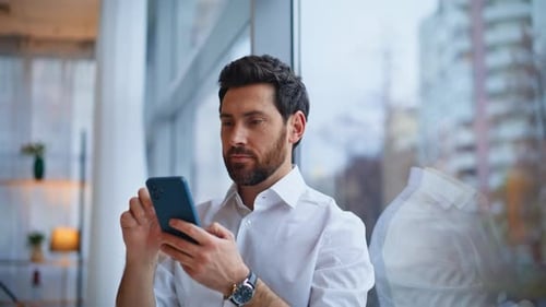 Closeup Smiling Man Texting Smartphone Enjoying Break at Panoramic Window Office