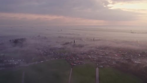 Aerial view of foggy sunrise over village with church and fields, Netherlands.