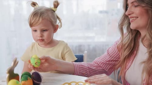 Mother and Child Interact with Colorful Easter Eggs on Table