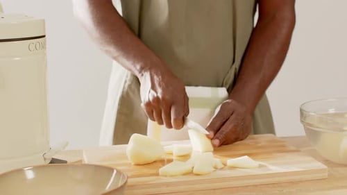 Afroamerikaner in Schürze pflückt geschältes Stück auf der Theke und schneidet Keile mit einem Messer für das Rezept