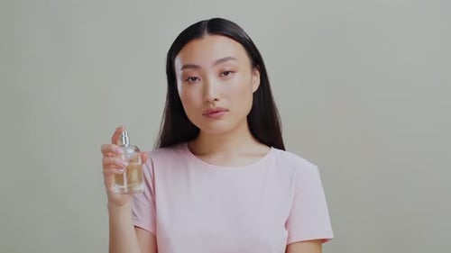 Woman Presents Perfume Bottle Against Plain Background