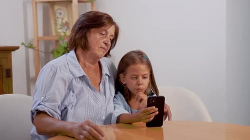 Happy Granddaughter and Grandmother Using Smartphone Together at Home