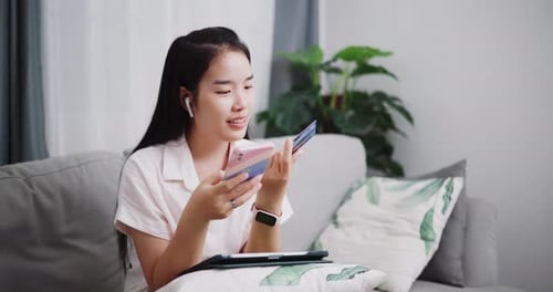 Young woman using her credit card and phone to shop online at home.