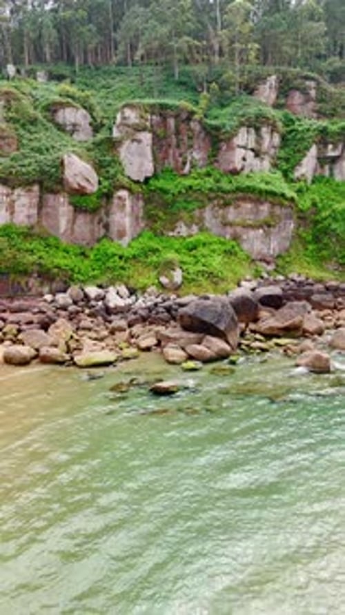 A pile of boulders lies at the mountain foot. Clear water of the sea splashes by the shore.