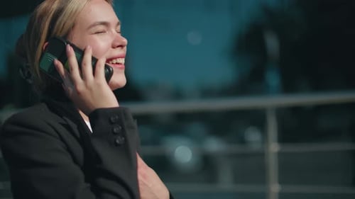 Young Woman Laughing on Phone Call Outside Modern Building in Sunlight