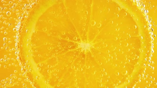 Eine Scheibe reifer Orange im Wasser sprudelt auf einem orangefarbenen Hintergrund.