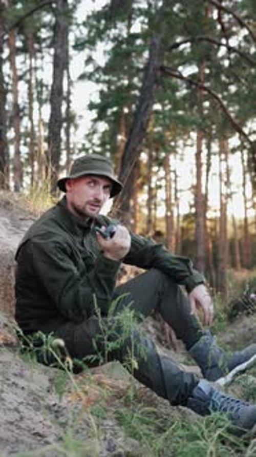 Military personnel uses walkie-talkie in woodland trench to stay in contact with headquarters.