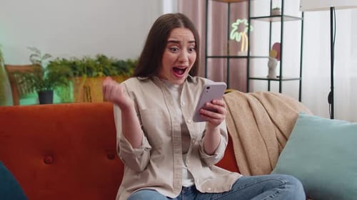 Woman Celebrates Good News While Using Phone on Couch