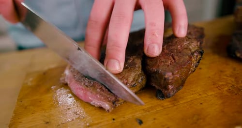 Close up view of Male hand with a knife slicing the juicy grilled Beef Steak on cutting Board.