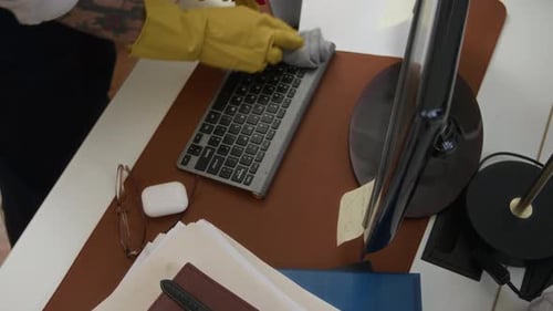Gloved Tattooed Hands of Janitor Wiping Computer and Keyboard on Office Table