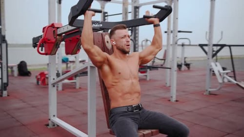 Muscular Man Trains Muscles Shoulders on a Special Simulator in the Outdoor Area