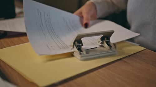 Person Using Hole Punch on Documents at Desk