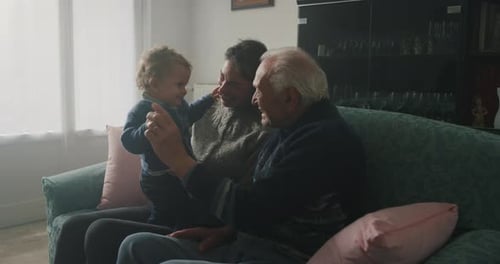 Cinematic shot of happy family: grandfather, daughter and grandson baby are having fun to pass tim